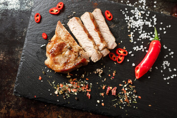 pork cooked in a pan and cut into pieces with spices on a dark stone background