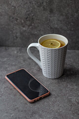 Fototapeta na wymiar smartphone and a cup of tea with lemon on a gray table