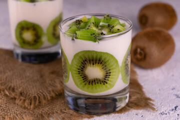 Two glasses with Greek yogurt with kiwi on a white plate.
Close-up.