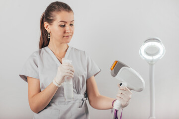 A woman tunes a laser hair removal machine. She holds a working part of the epilator in her hands and poses for a photo. It is located in a modern beauty salon. Body Care. Underarm Laser Hair Removal.