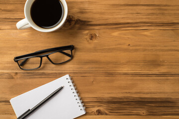 Above overhead close up view photo picture of mug of strong coffee eyeglasses open clear notebook with black pen isolated light color brown background with copy space