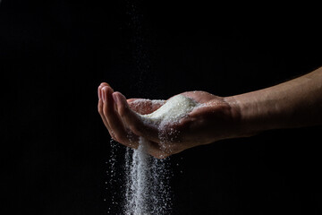 Sugar on a black background. Sugar pours from a man's hand. Excessive sugar intake