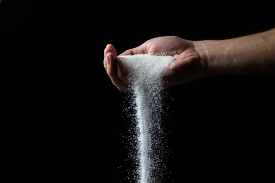 Sugar on a black background. Sugar pours from a man's hand. Excessive sugar intake