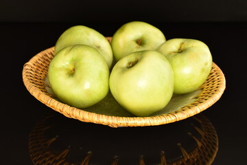Several natural green apples by Renet Simirenko with a ceramic plate, close-up, isolated on black.