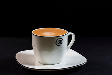 Coffee with milk in porcelain cup and saucer.The photograph is a horizontal shot taken in a studio under artificial lighting.