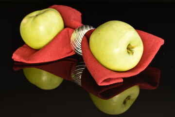 Two natural green apples by Renet Simirenko with a red linen napkin, close-up, isolated on black.