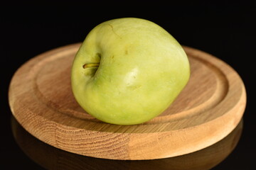 One natural green apple by Renet Simirenko on a wooden tray, close-up, isolated on black.