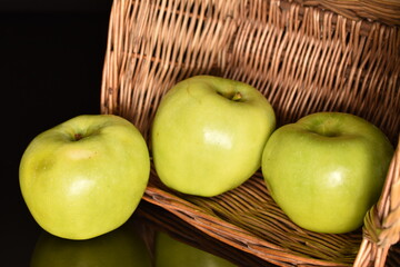 Three natural green apples by Renet Simirenko with a basket of vines, close-up, isolated on black.