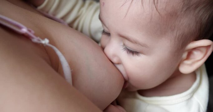 Mother breastfeeding her newborn baby on sofa. Milk from mother's breast is a natural medicine to baby. family, food, child, eating and parenthood concept. slow motion