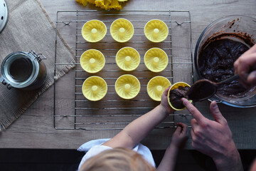 Yellow form for baking homemade muffins. Hands of child and father prepare chcoalte cupcakes for easter. Healthy food and pastry in a bowl. Top view.