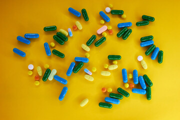 Pharmaceutical colorful pills and capsules on yellow background.  A large number of tablets on the...
