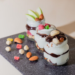 Sweet tasty milk curd creamy food in a glass jar of homemade breakfast. Cheesecake, English Trifle, Eton dessert, tiramisu, zuppa Inglese with nuts, almonds, cashews, hazelnuts, candied fruits 