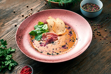 Delicious coconut and lentil cream soup with croutons and jamon in a red plate on a wooden background. Restaurant food. Close up view