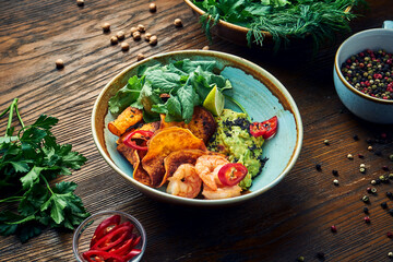 Appetizing mexican appetizer - avocado guacamole with shrimps, vegetable chips and cilantro in a bowl on a wooden background. Close up view