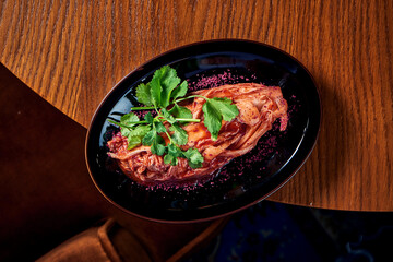 A traditional Korean dish is spicy Chinese cabbage kimchi with spices and hot sauce, served in a black plate on a wooden background. View from above