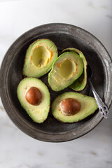 Four pieces of avocado, one of which is peeled, in an old metal plate.