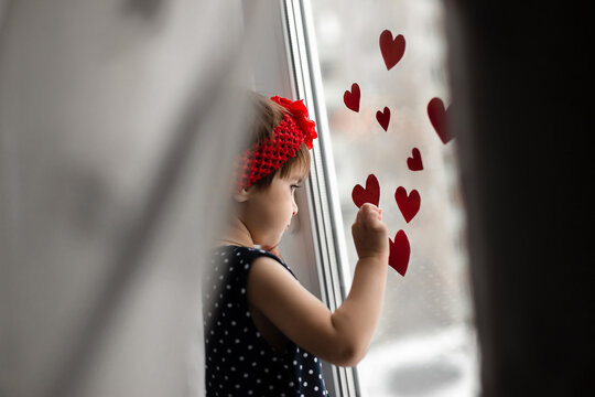 Little Girl With Small Red Paper Hearts Near The Window.