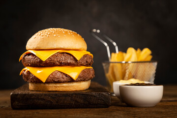 Tasty hamburger with french fries and sauces on dark background. - obrazy, fototapety, plakaty