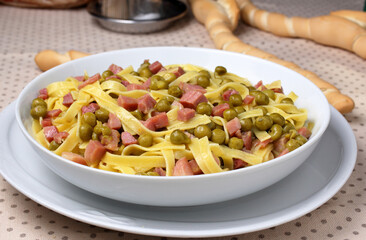 Piatto di tagliatelle con piselli e prosciutto cotto. Tavola apparecchiata per il pranzo. Pasta tradizionale italiana.