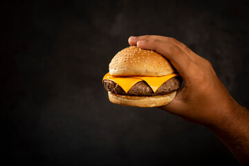 Hand holding hamburger on dark background.
