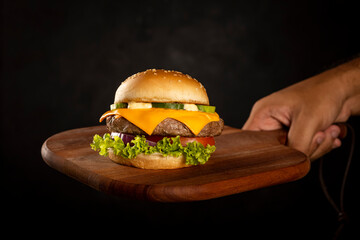 Tasty hamburger on wooden board on dark background. - obrazy, fototapety, plakaty