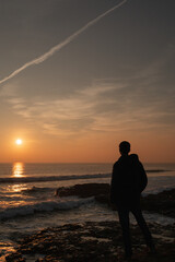 Man looking at the sunset with hand in pocket in the Atlantic ocean in Portugal