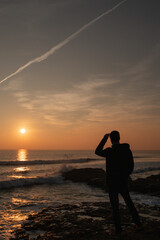 Fototapeta na wymiar Man watching the sunset lifting his glasses in the Atlantic ocean in Portugal