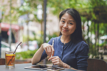 Portrait of a cheerful Asian woman working remotely while sitting in a coffee shop