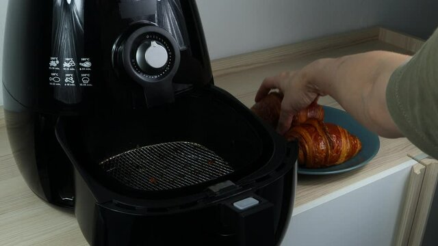 homemade croissant is taken out of the black air fryer or oil free fryer appliance on the wooden table with background of white cement wall in the kitchen for being breakfast in the moring