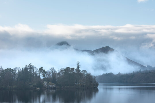 Dramatic landscape image looking across Derwentwater in Lake District towards Catbells snowcapped mountain with thick fog rolling through valley © veneratio