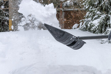 somebody is throwing snow with a black plastic shovel, snow removal tool, shoveler cleaning snow out of a road in a winter day outdoors, thick snow after a snowfall