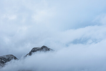Epic Winter landscape image of view from Side Pike towards Langdale pikes with low level clouds on mountain tops and moody mist swirling around