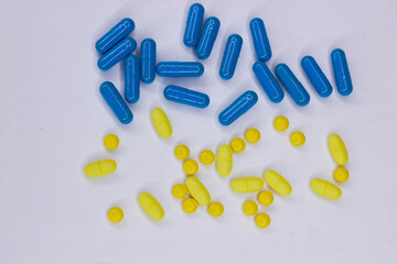 Pharmaceutical blue and yellow pills and capsules on a white background. A large number of tablets on the surface.
The concept of modern treatment, pharmacy, healthcare. View from above.