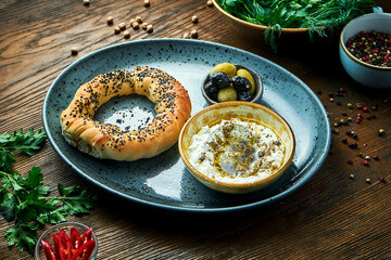 Classic Turkish breakfast - simit with feta cheese mousse with olive oil and spices, served on blue plate with olives. Wood background. Restaurant food. Simit - bagel with poppy seeds or sesame seeds