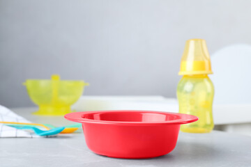 Red plastic bowl on grey marble table indoors, space for text. Serving baby food