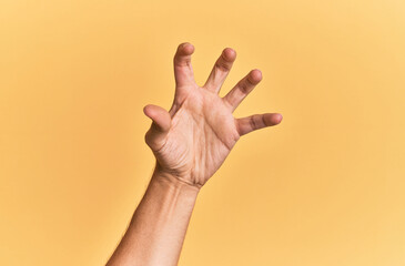 Arm and hand of caucasian man over yellow isolated background grasping aggressive and scary with fingers, violence and frustration