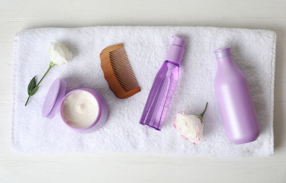 Different hair products, towel and comb on white wooden table, top view