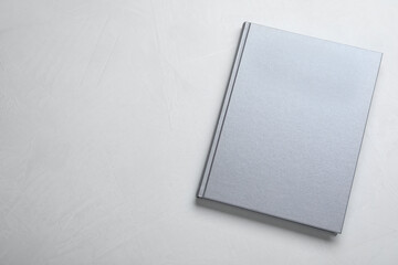 Closed grey book with hard cover on light grey table, top view. Space for text