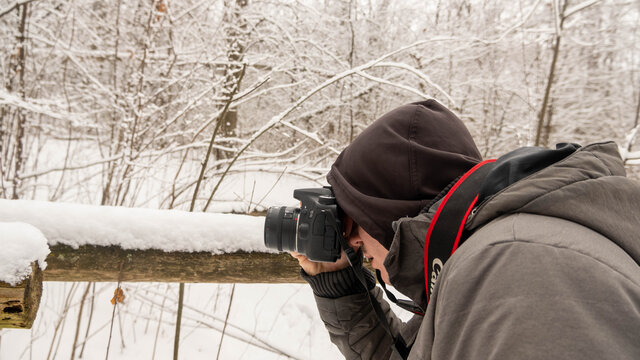 London, Canada, January 19, 2021: Editorial photo of a man in a grey jacket taking pictures outside. Winter day in London, Canada with snow on trees and ground.