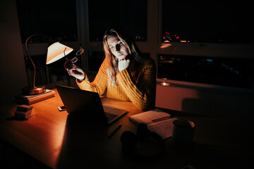 Caucasian business woman holding spectacles working late at night reading online article in home office