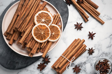 Fototapeta na wymiar Aromatic cinnamon sticks, dry orange and anise on white marble table, flat lay