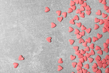 Pink heart shaped sprinkles on grey table, flat lay. Space for text