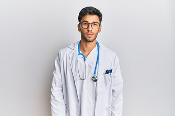 Young handsome man wearing doctor uniform and stethoscope relaxed with serious expression on face. simple and natural looking at the camera.