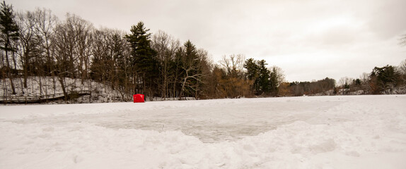 Cleared off ice skating rink on frozen pond in Dorchester, Canada. White snow moved for ice hockey rink on frozen water. Red ice fishing tent on frozen lake