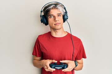 Young hispanic man playing video game holding controller relaxed with serious expression on face. simple and natural looking at the camera.