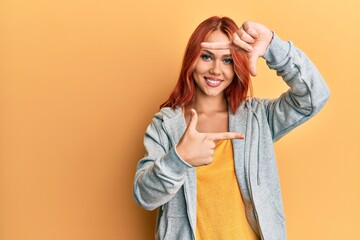 Young beautiful redhead woman wearing casual sporty sweatshirt smiling making frame with hands and fingers with happy face. creativity and photography concept.