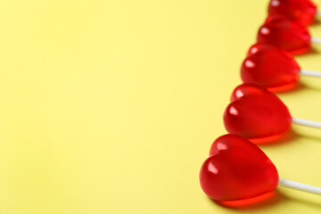 Sweet heart shaped lollipops on yellow background, closeup view with space for text. Valentine's day celebration