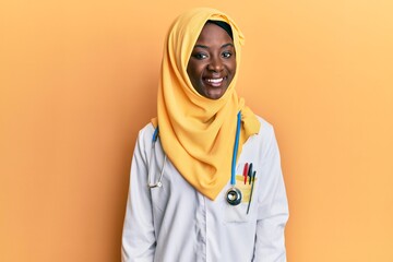 Beautiful african young woman wearing doctor uniform and hijab with a happy and cool smile on face....