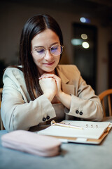 Beautiful young woman in suit writing her business plans while drinking coffee on break time