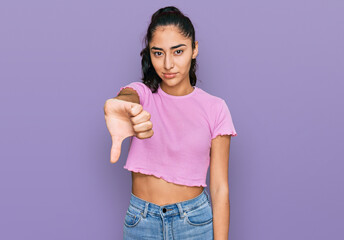 Hispanic teenager girl with dental braces wearing casual clothes looking unhappy and angry showing rejection and negative with thumbs down gesture. bad expression.